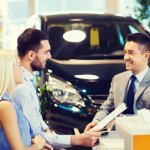 happy couple with car dealer in auto show or salon